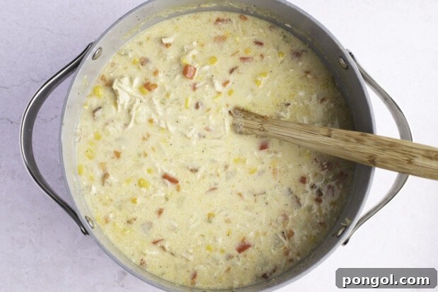 Overhead view of chicken corn chowder in a large, heavy-bottomed pot with wooden spoon on a white background.