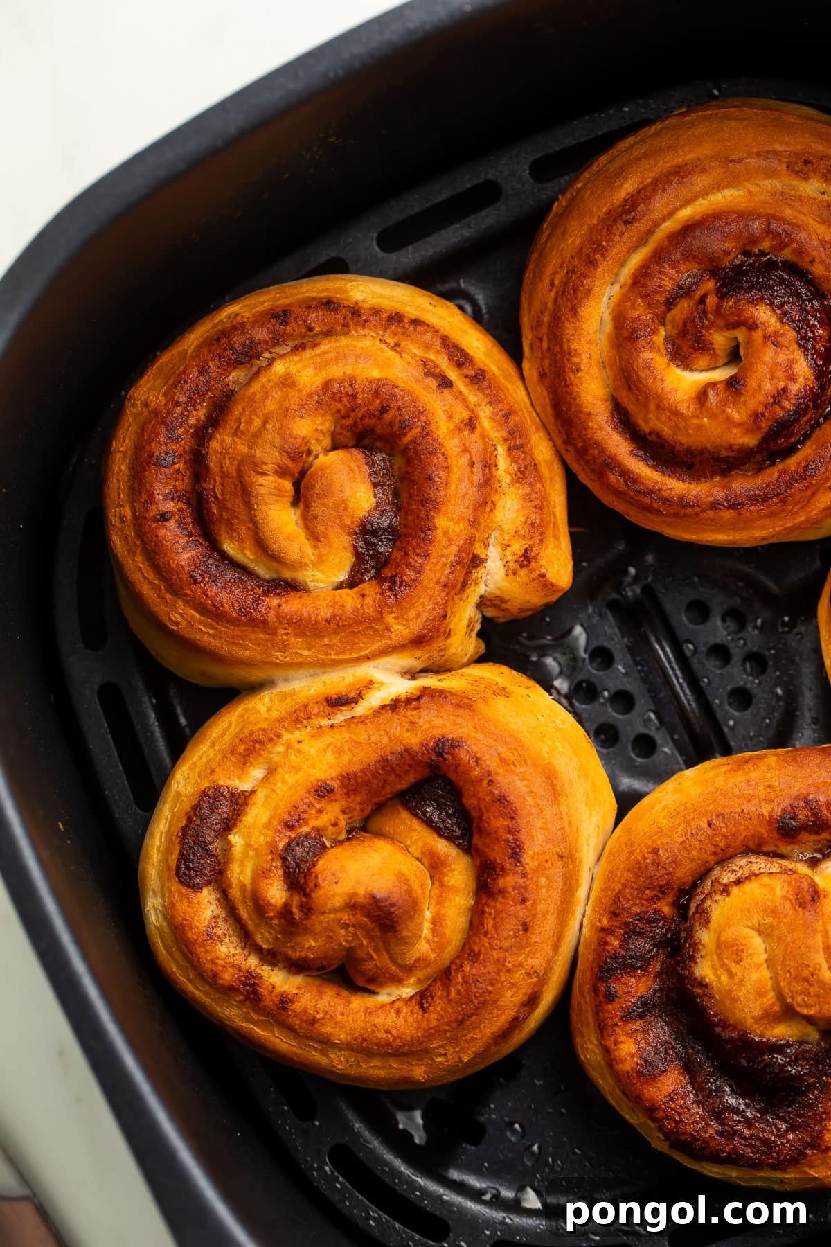 Close-up shot of several un-iced cinnamon rolls in an air fryer basket, showcasing their perfect golden-brown swirl and inviting texture.