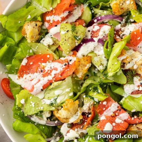 Overhead, close-up view of a smoked salmon bagel salad in a white bowl.