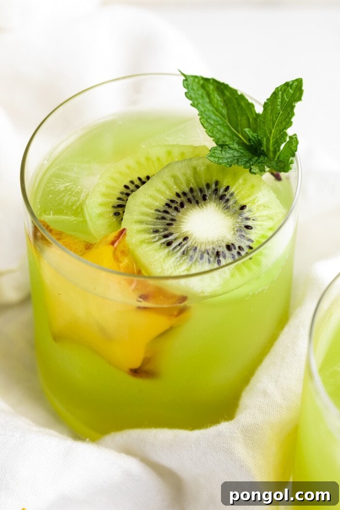 Close-up, 3/4 angle view of a glass of lime green kiwi starfruit refresher with slices of kiwi and starfruit, showcasing its vibrant color and fresh ingredients.