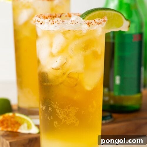 Close up of two tall salt-rimmed glasses of chelada in front of green beer bottles