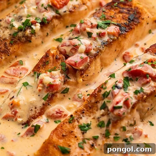 Extreme close-up of pan-seared salmon fillet showing crispy golden crust with creamy red pepper parmesan sauce.