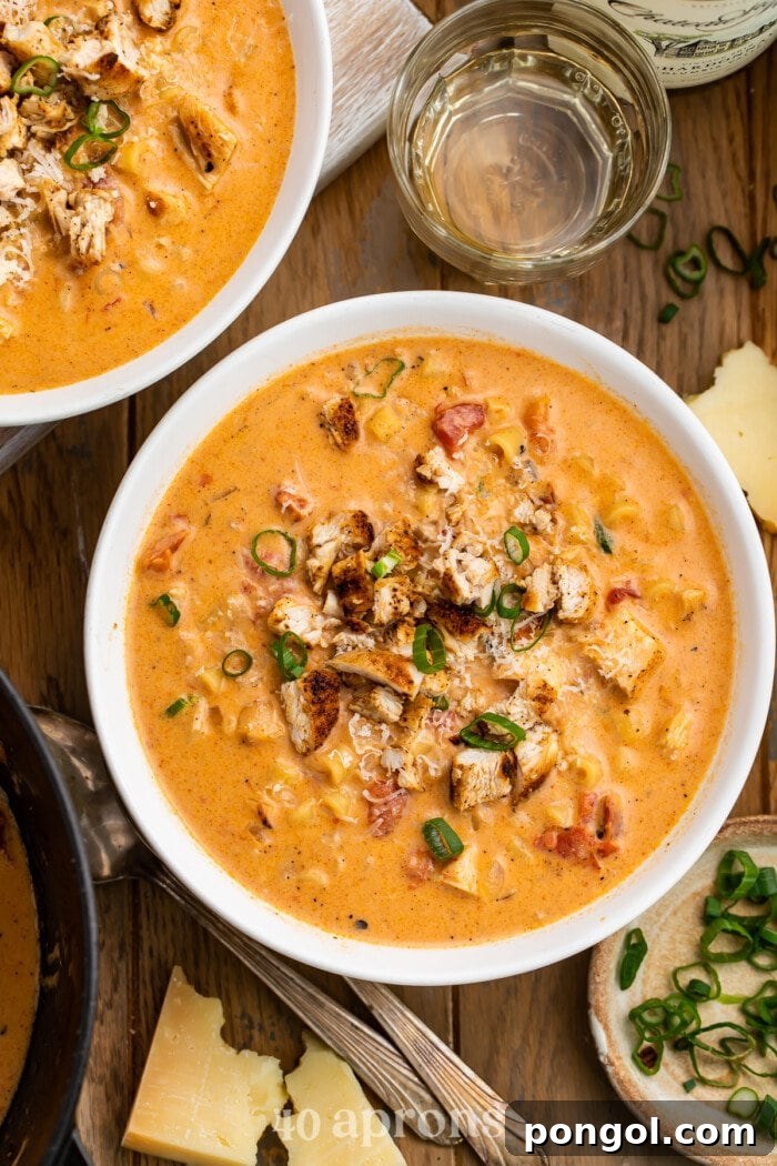 A beautiful overhead shot of a single bowl of creamy Cajun chicken pasta soup, garnished with fresh green onions, sitting on a rustic wooden table with a partial second bowl in view.