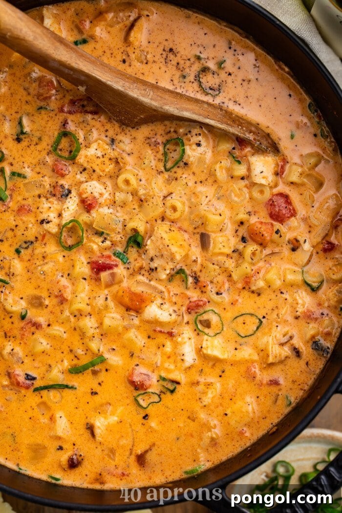 A large, rustic Dutch oven filled to the brim with creamy Cajun chicken pasta soup, with a wooden spoon resting inside, ready to serve.