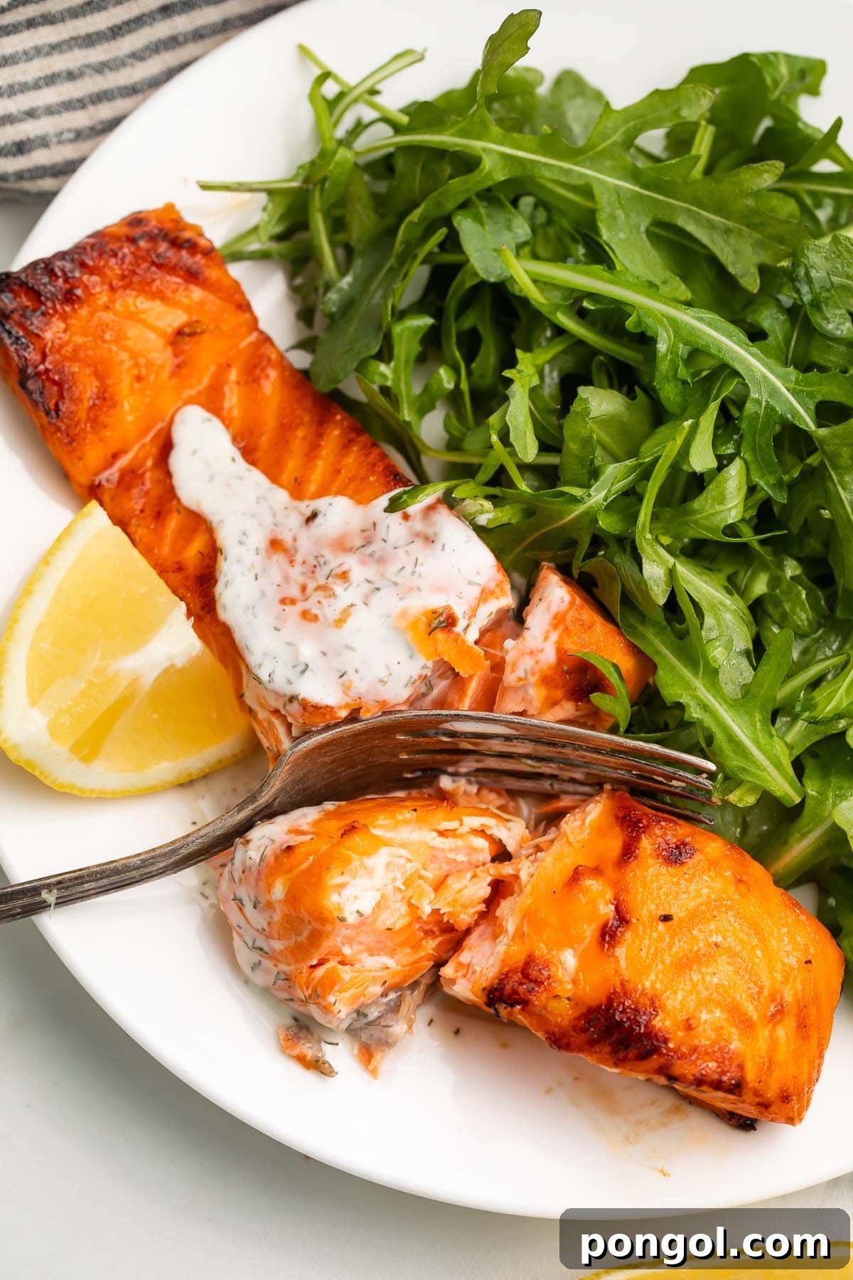 A salmon fillet, cooked in an air fryer, topped with a creamy dill sauce and served with a small salad.