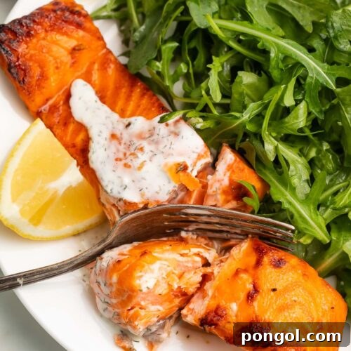 A salmon fillet, cooked in an air fryer, topped with a creamy dill sauce and served with a small salad.
