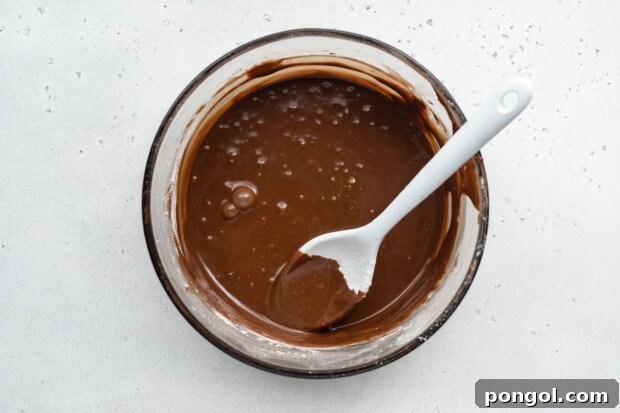 Overhead view of chocolate icing for chocolate gluten-free donuts in a large glass mixing bowl with a spoon.
