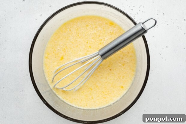 Overhead view of wet ingredients for gluten-free donuts in large glass bowl with whisk.