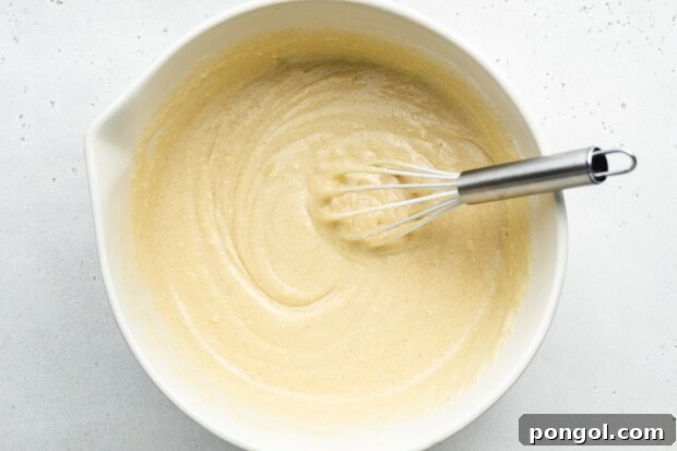 Overhead view of vanilla gluten-free donut batter in large glass mixing bowl with metal whisk.