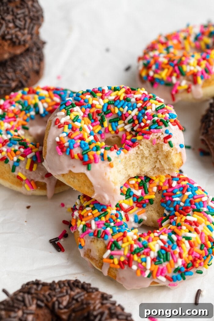 3/4 angle photo of a stack of vanilla donuts with rainbow sprinkles, with one bite taken out of one donut, highlighting the soft interior.