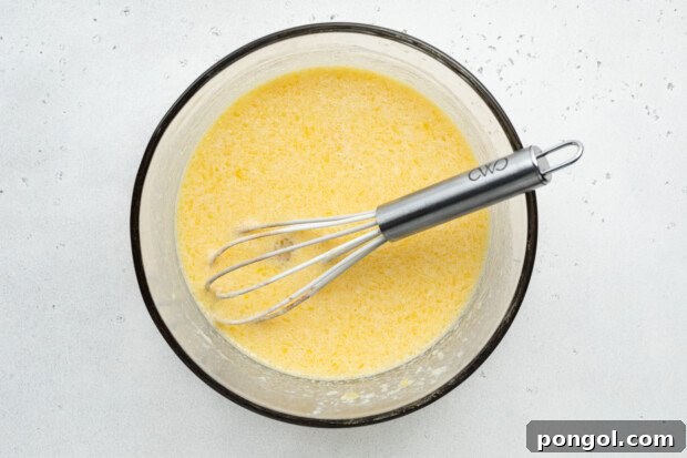 Overhead view of wet ingredients for gluten-free donuts in large glass bowl with whisk.