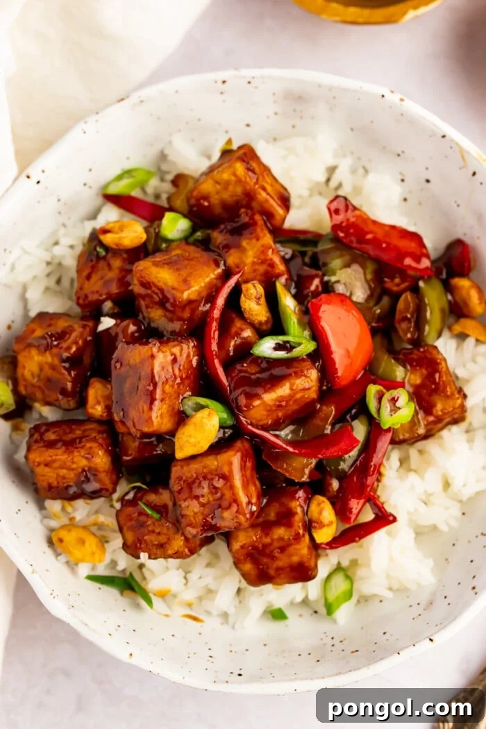 Overhead view of kung pao tofu with stir-fried veggies and white rice in a white bowl.