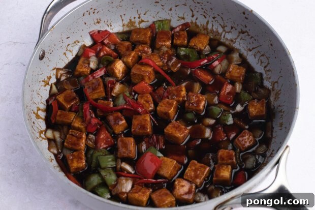 Kung Pao tofu with sauce and veggies in a large grey skillet against a white background.