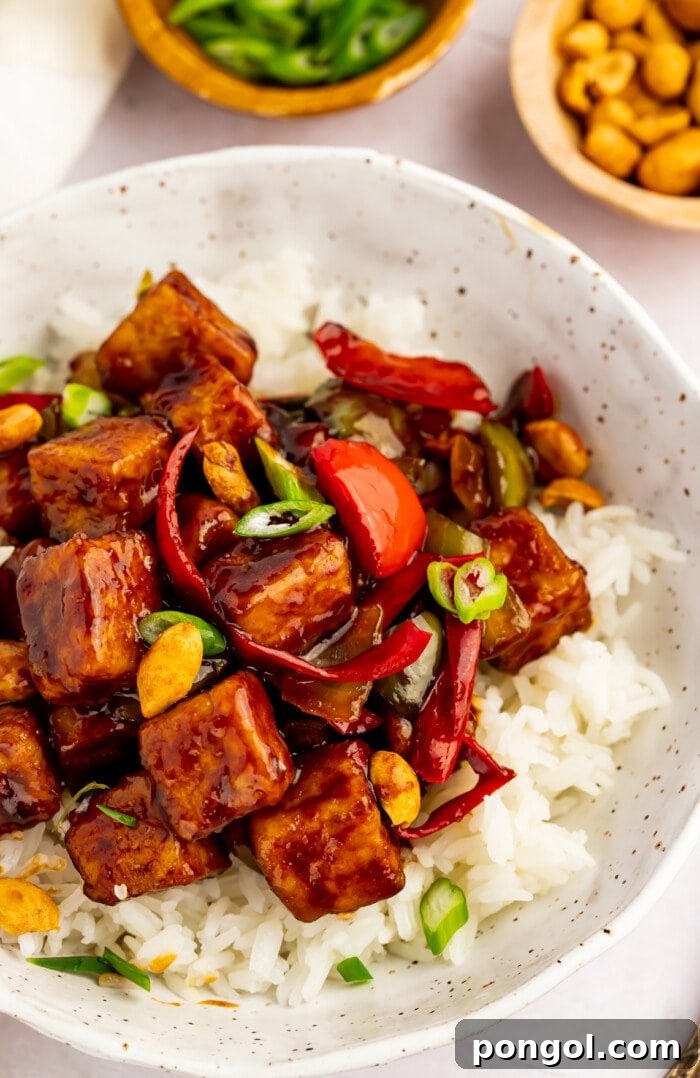 Overhead view of kung pao tofu and stir-fried veggies in a bowl with white rice and green onions.