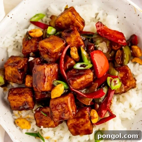 Overhead view of kung pao tofu with stir-fried veggies and white rice in a white bowl.