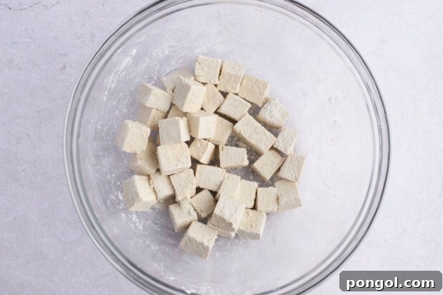 Cornstarch-coated tofu cubes in large glass mixing bowl on white background.