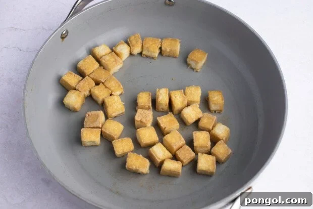 Cooked tofu cubes in large grey skillet on white background.