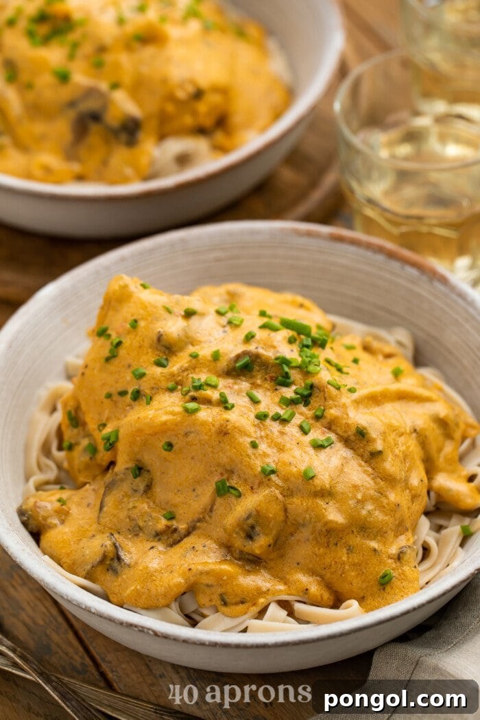 3/4-angle view of two bowls of Crockpot angel chicken served over a bed of pasta with a glass of water, garnished with fresh chives.