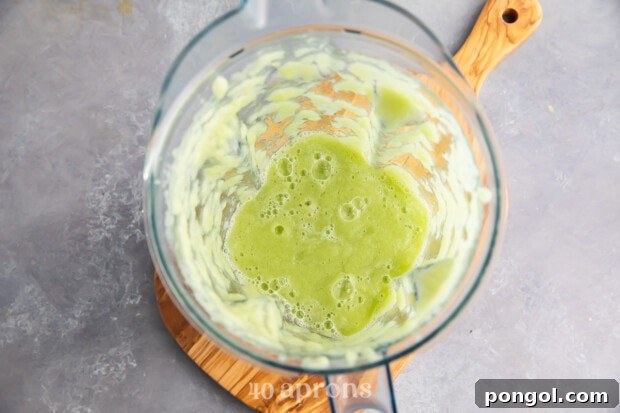 Overhead view of cucumber juice in glass blender on wooden board.
