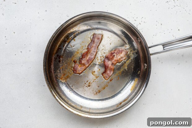 The Ultimate Breakfast Stack 5 Bacon cooking in a large silver skillet, sizzling and browning.