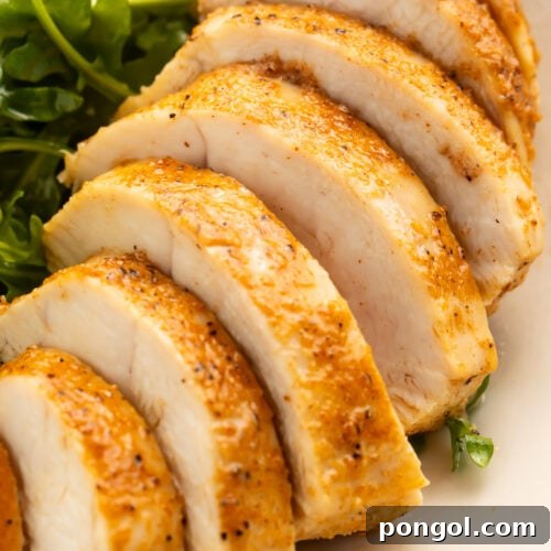 A juicy, Instant Pot chicken breast on a plate with a small salad. The chicken is sliced into 7 slices.