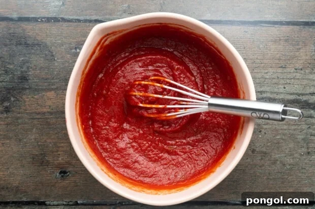 Overhead view of bright red pizza sauce in a white mixing bowl with a whisk, showing its smooth consistency.