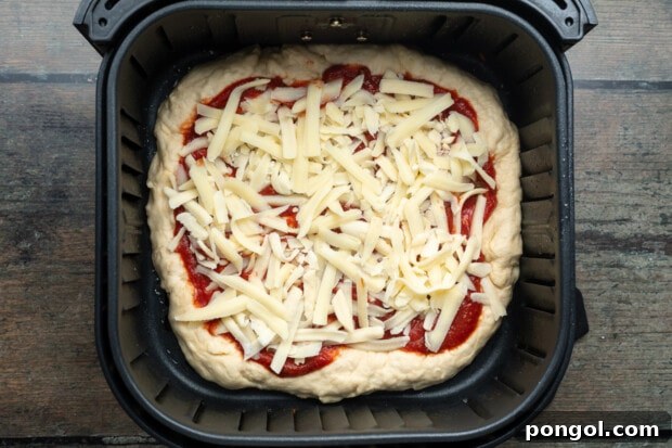 Overhead view of an unbaked air fryer pizza topped with pizza sauce and shredded cheese in an air fryer basket, ready for cooking.