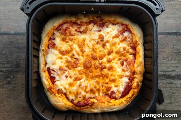 Overhead view of a fully baked air fryer pizza, golden and bubbly, topped with pizza sauce and shredded cheese in an air fryer basket, sliced and ready to serve.