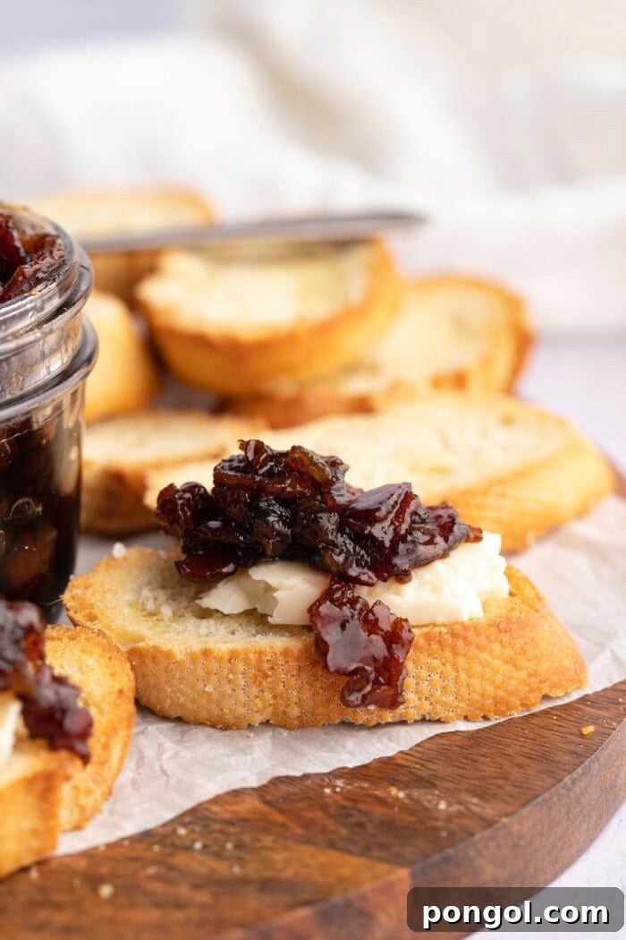 Side view of bacon jam atop crostini and cheese on a wooden cutting board.