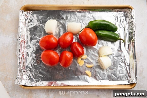 Roma tomatoes, jalapeños, garlic, and onions on a baking sheet lined with aluminum foil.