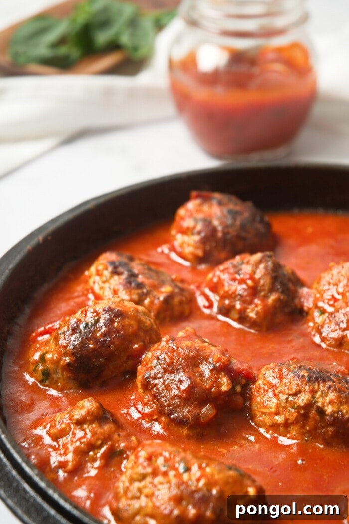 Wholesome Whole30 Meatballs in Rich Marinara 2 Whole30 Italian meatballs simmering in a rich marinara sauce within a rustic cast-iron skillet, ready to be served.