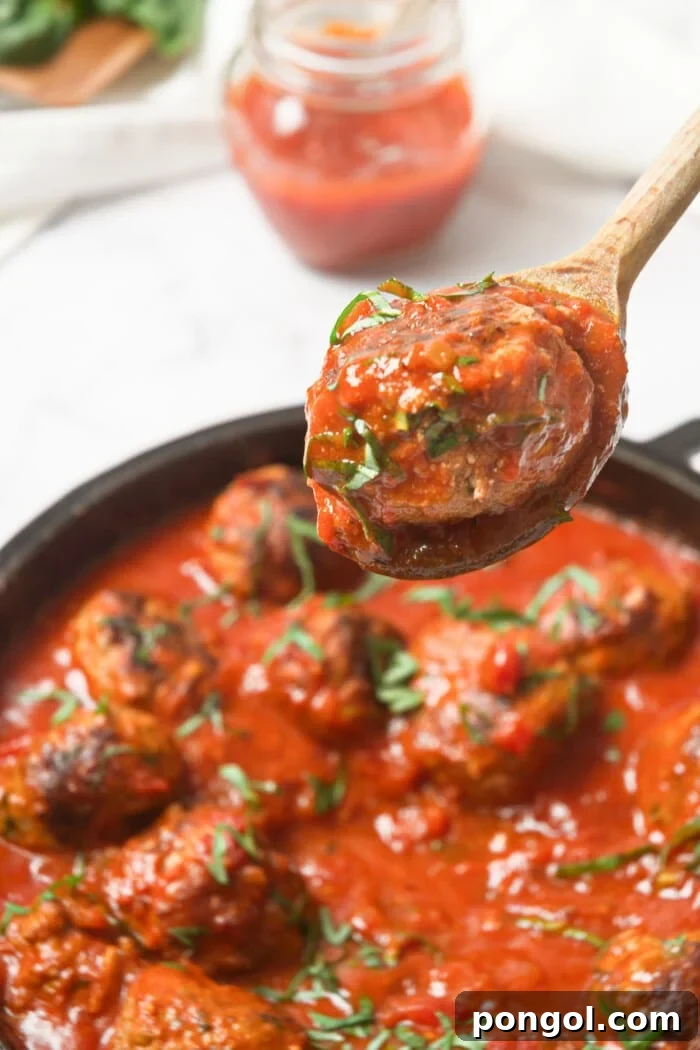 Wholesome Whole30 Meatballs in Rich Marinara 3 A Whole30 Italian meatball being carefully lifted from a cast iron skillet, showcasing its golden-brown exterior and the rich marinara sauce.