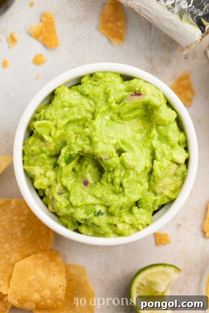 Close-up view of a ramekin with Chipotle guacamole surrounded by lime tortilla chips, showcasing its vibrant green color and smooth texture.