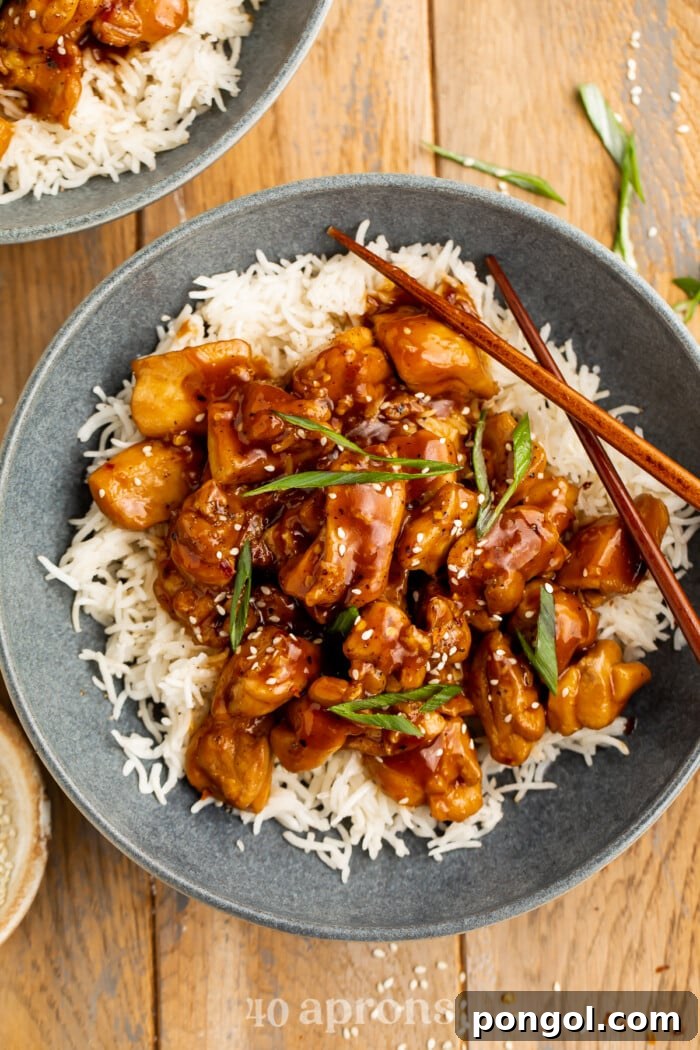 Sticky Bourbon Glazed Chicken 2 Overhead view of a dark blue-grey bowl of white rice topped with Bourbon Chicken and chopped green onions.