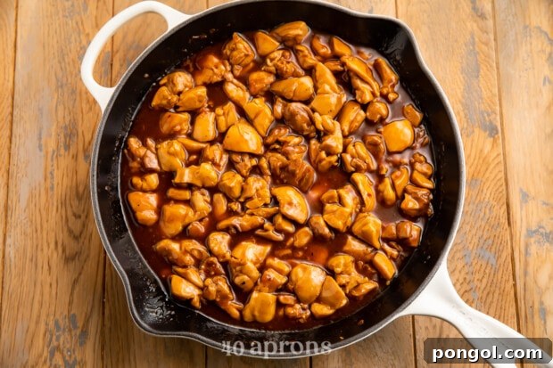 Sticky Bourbon Glazed Chicken 8 Overhead view of a large skillet with chicken thigh pieces in bourbon sauce on a wooden table.