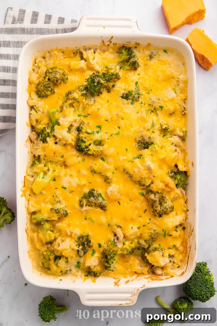 Overhead view of a white rectangular casserole dish full of cheesy chicken, broccoli, and rice, freshly baked and golden.
