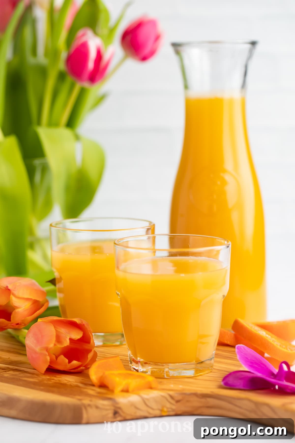 Tropical Homemade Disney POG Juice 2 Side view of a glass of bright orange POG juice with a carafe of POG Juice and another glass in the background.