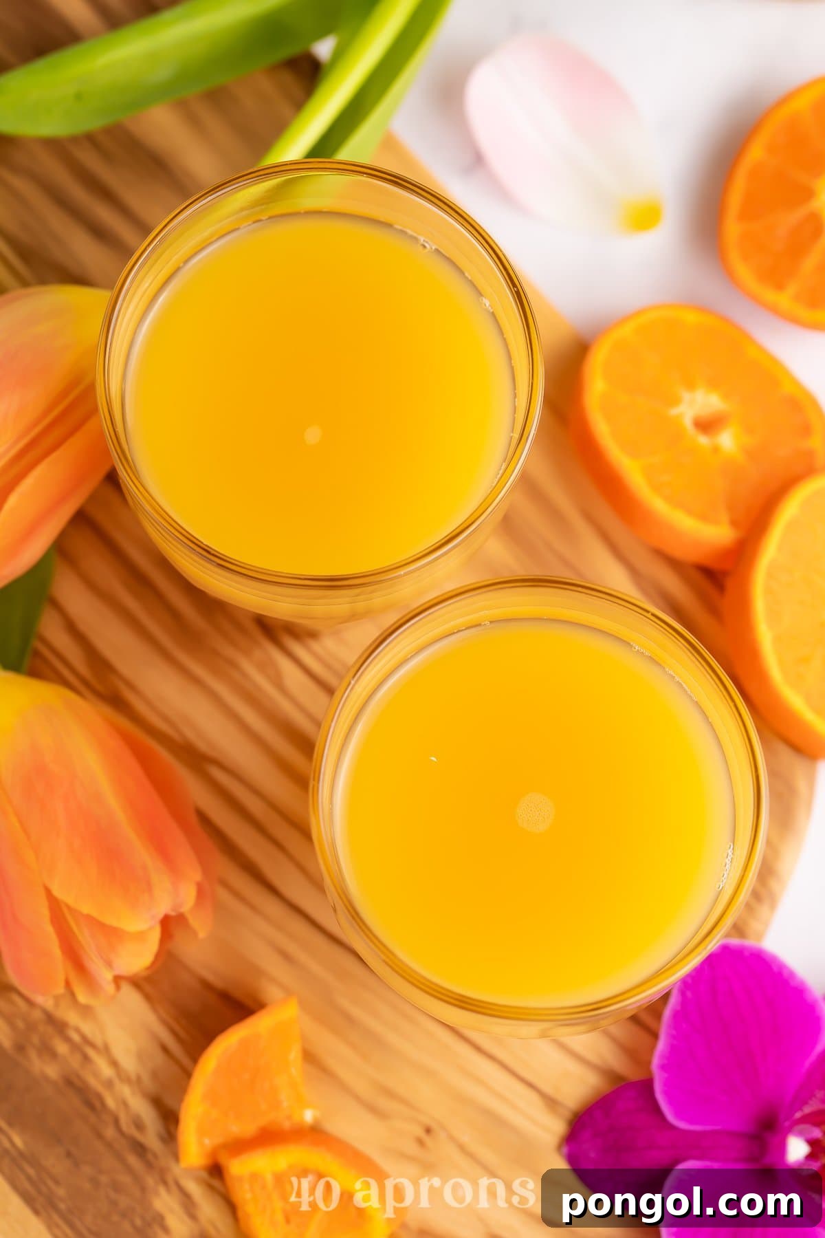 Tropical Homemade Disney POG Juice 3 Overhead view of two glasses of POG juice on a wooden serving tray with bright pink tropical flowers.