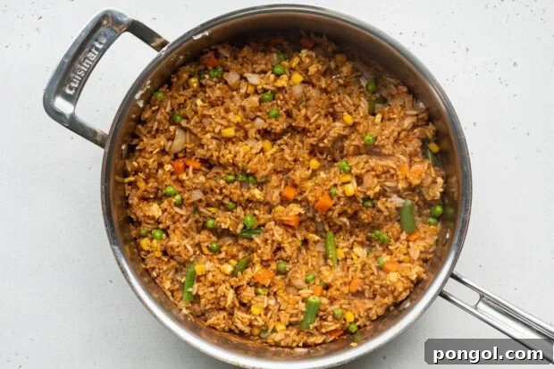 Overhead view of vegetable fried rice, rich with egg and soy sauce, cooking in a large skillet.