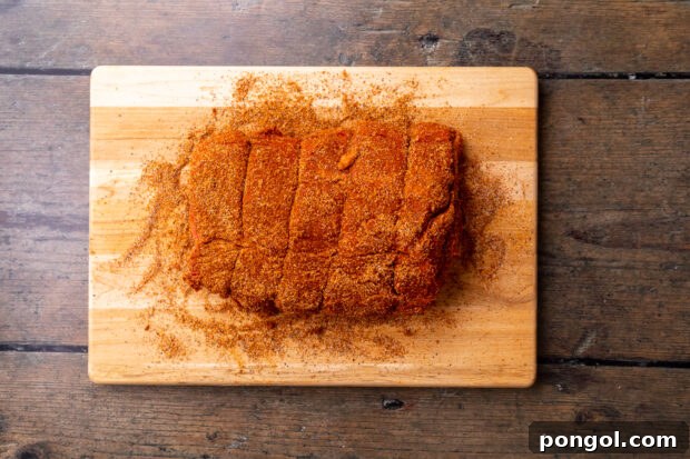 Overhead view of uncooked beef roast covered in taco seasoning on a wooden cutting board.