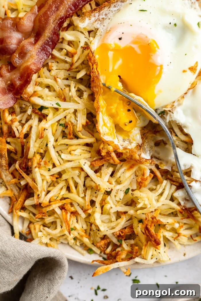 Golden Air Fryer Hashbrowns with Fiery Chipotle Ketchup 2 Close-up view of air fryer hashbrowns on a plate with bacon and an egg.