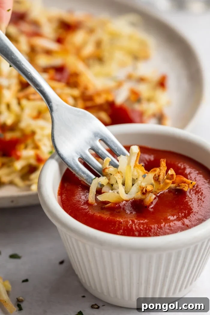 Golden Air Fryer Hashbrowns with Fiery Chipotle Ketchup 3 Air fryer hashbrowns on a fork being dipped into a small ramekin of chipotle ketchup.