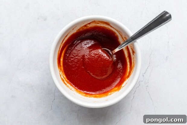 Golden Air Fryer Hashbrowns with Fiery Chipotle Ketchup 8 Overhead view of a small white ramekin with ketchup and chipotle adobo sauce with a spoon.