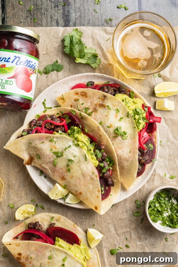 Tangy Beet Tacos 2 Overhead view of two pickled beet tacos on a plate surrounded by garnish and a jar of pickled beets, highlighting their vibrant colors.