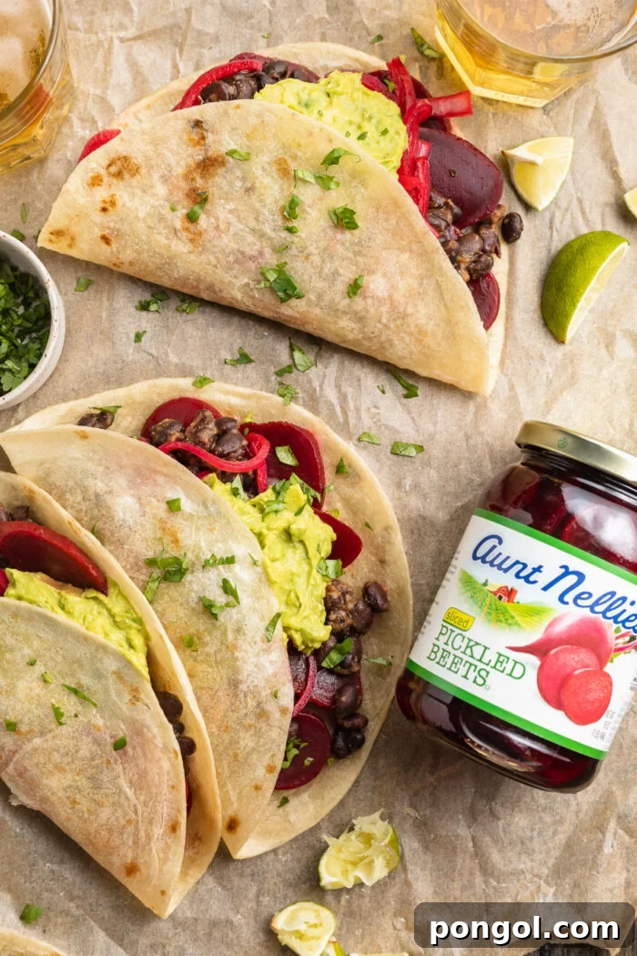 Tangy Beet Tacos 3 Overhead view of 3 pickled beet tacos on parchment paper with a jar of pickled beets, showcasing the beautiful arrangement.