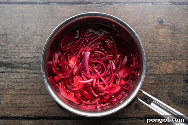 Tangy Beet Tacos 6 Overhead view of red onions pickling in a silver saucepan, showing the vibrant process.
