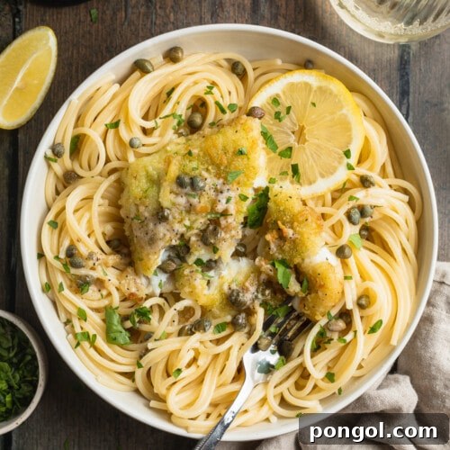 Overhead view of a bowl of potato-crusted cod piccata with spaghetti noodles, lemon slices, capers, and chopped parsley.