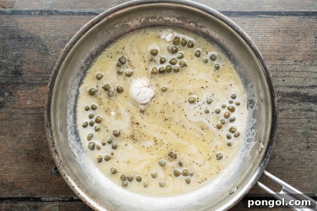 Overhead view of white wine, capers, flour, salt, and pepper in a large silver skillet.