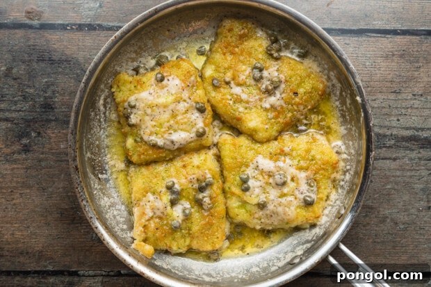 Overhead view of 4 potato-crusted cod fillets in a large skillet with a white wine sauce.
