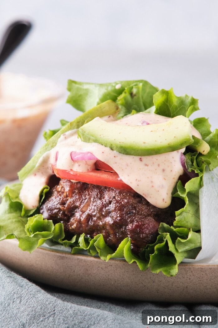 Side view of a Whole30 burger with spicy mayo wrapped in lettuce with tomatoes and red onion.